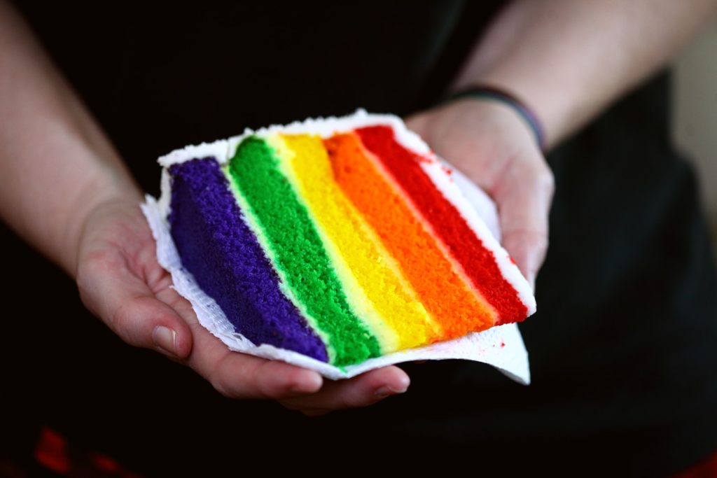 Person holding rainbow-themed cake slice. Photo by Sharon McCutcheon on Unsplash.
